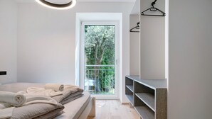 A modern bedroom with a bed, a window with a view of trees, a hanging light fixture, and built-in shelves. - Apartment 'Haus Weinblick Apt 3' with Mountain View, Wi-Fi, and Air Conditioning (Margreid)
