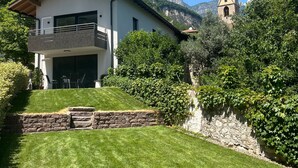 A modern house with a balcony, a stone wall, and a church in the background. - Apartment 'Haus Weinblick Apt 3' with Mountain View, Wi-Fi, and Air Conditioning (Margreid)