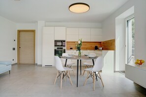 Une cuisine moderne avec des meubles blancs, une table à manger avec des chaises et une grande fenêtre.