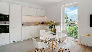 Een moderne keuken met witte kastjes, een eettafel met stoelen, een vaas met bloemen en uitzicht op een berg door een groot raam.