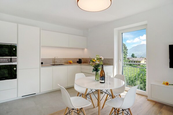 Una cocina moderna con armarios blancos, una mesa de comedor con sillas, un jarrón con flores y una vista de la montaña a través de un ventanal grande.