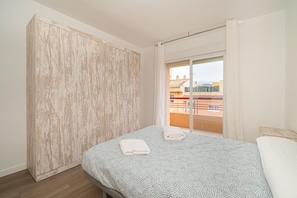 Une chambre à coucher comprenant un lit, une armoire et un balcon avec vue sur les immeubles.