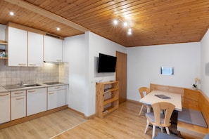 A modern kitchen with wooden cabinets, a built-in oven, a sink, and a dining area with a table and chairs.