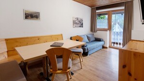 Une pièce avec une table en bois, deux chaises, un canapé et une fenêtre avec des rideaux.