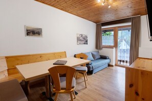 Huoneessa on puinen pöytä, kaksi tuolia, sohva ja ikkuna, jossa on verhot.