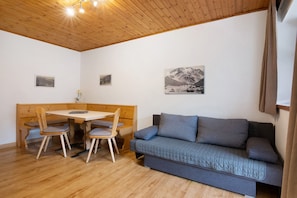 A room with a wooden ceiling, a wooden bench, a table with chairs, and a grey sofa.
