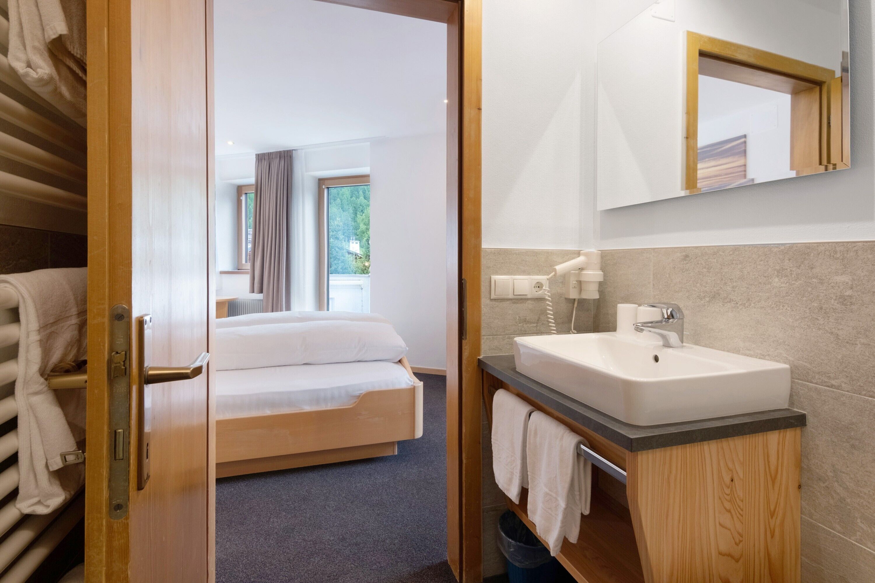 Une chambre d’hôtel avec un lit, une salle de bain comprenant un lavabo et un miroir, et une vue sur l’extérieur.