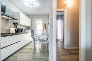 Une cuisine moderne avec des meubles blancs, une table à manger avec des chaises et une porte visible donnant sur une autre pièce.