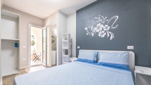 Un dormitorio con cama, armario, mesita de noche, estante y pared con diseño floral.