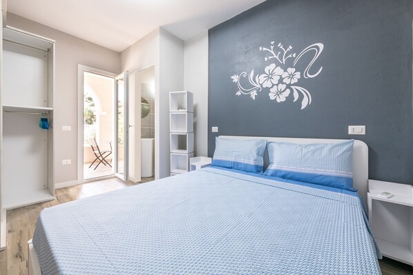 Une chambre à coucher comprenant un lit, une armoire, une table de chevet, une étagère et un mur orné d’un motif floral.
