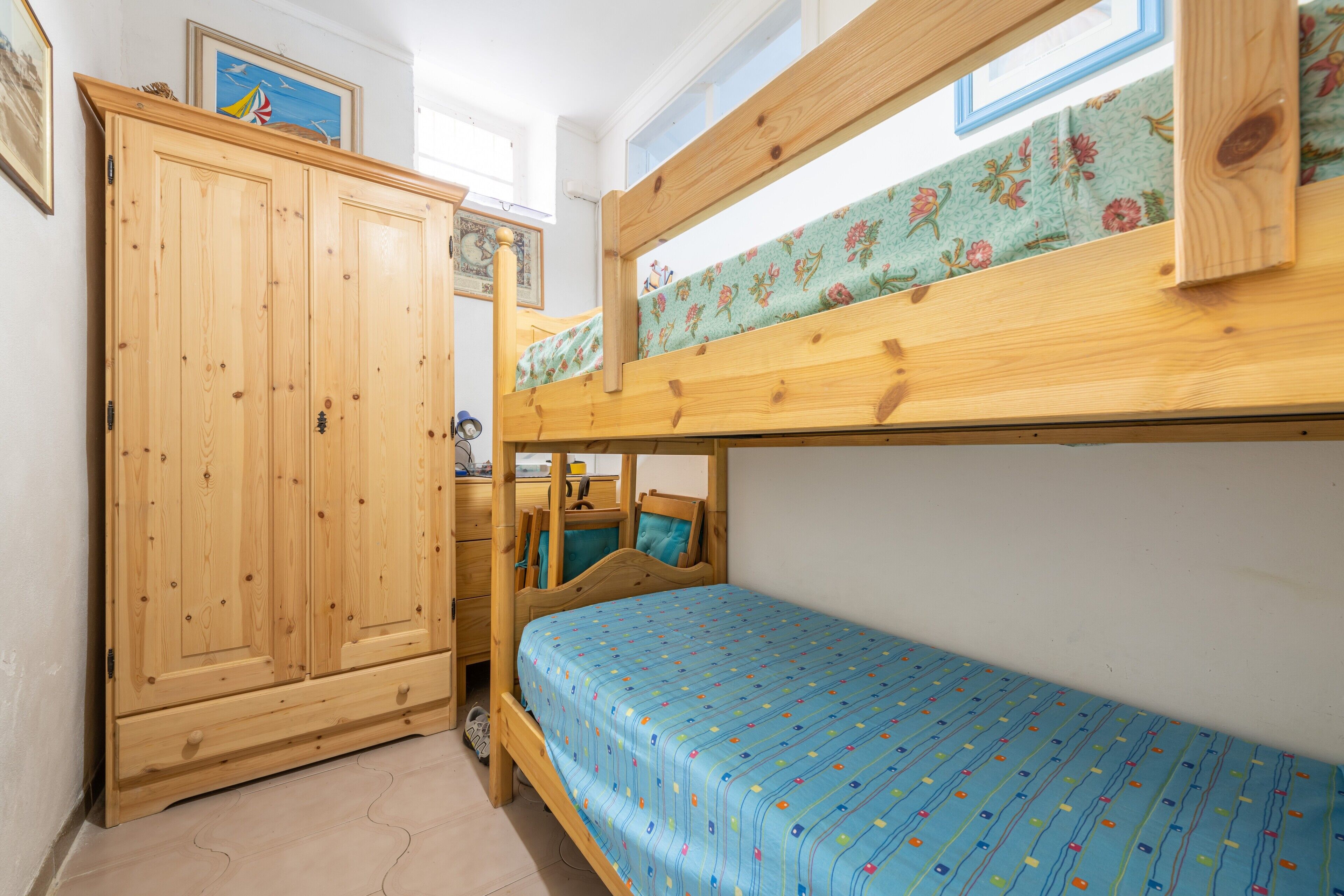 A bunk bed with a floral-patterned mattress, a wooden wardrobe, and a small desk with a chair.