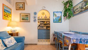 Una habitación acogedora con un sofá azul, una mesa de comedor con mantel azul y una zona de cocina con armarios azules y suelo de baldosas.