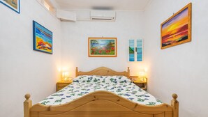 Un dormitorio con cama de madera, mesita de noche, aire acondicionado de pared y cuadros enmarcados.