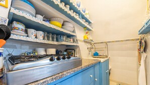 Una cocina con armarios azules, una estufa de acero inoxidable y repisas con vajilla y cristalería.