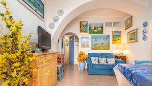 Una sala de estar con un sofá azul, un televisor, un mueble de madera y un jarrón con flores.