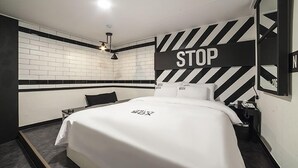 A modern hotel room with a large bed, a "STOP" sign on the wall, and a small table with a lamp. - Gunsan Hotel Box (Gunsan)