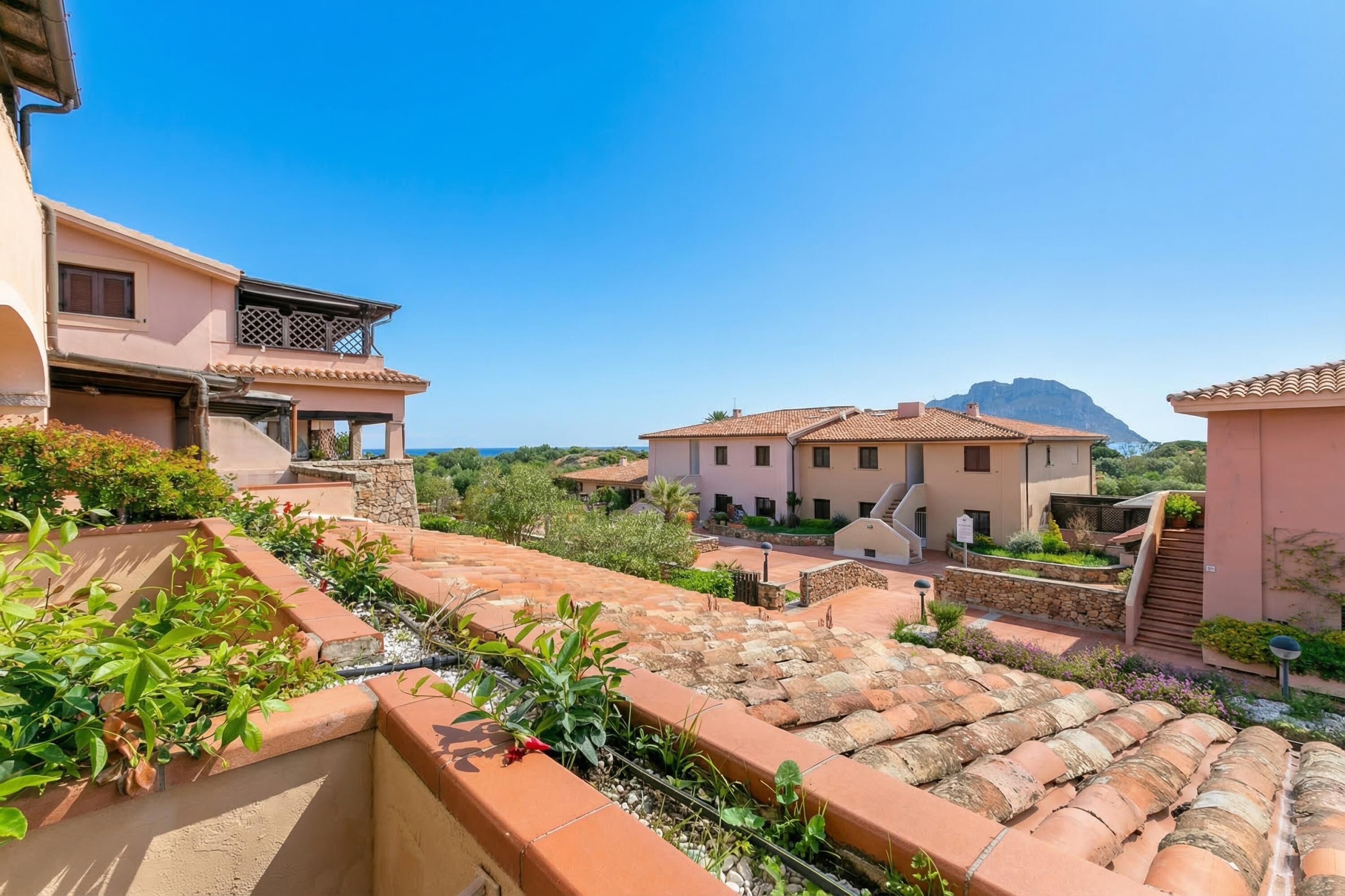 Zona residencial con tejados de tejas de arcilla, muros de piedra y abundante vegetación.