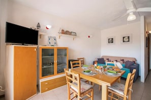 Spiseområde med et træbord, stole og et fjernsyn på et skab.