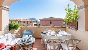 A balcony with a table set for two, chairs, and a view of buildings and mountains.