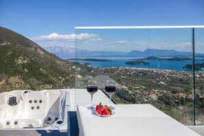 Una vasca idromassaggio con due bicchieri di vino rosso e un piatto di fragole su un balcone con vista su una cittadina costiera.