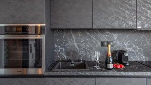 A kitchen with a built-in oven, a marble backsplash, a sink, a wine bottle, and a glass. - Villa "Desun Suites Grey" with Sea View, Pool & Wi-Fi (Leukada)