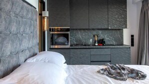 A modern hotel room with a bed, a built-in minibar, a small kitchen area, and a large window. - Villa "Desun Suites Grey" with Sea View, Pool & Wi-Fi (Leukada)