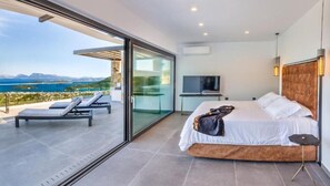 A modern bedroom with a bed, a TV, and a balcony with a view.