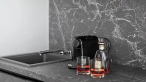 Eine Küchenarbeitsplatte mit einer Kaffeemaschine, zwei Gläsern roter Flüssigkeit und einer Flasche.