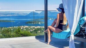 Una persona sentada en un balcón con vista a una masa de agua y tierra distante.