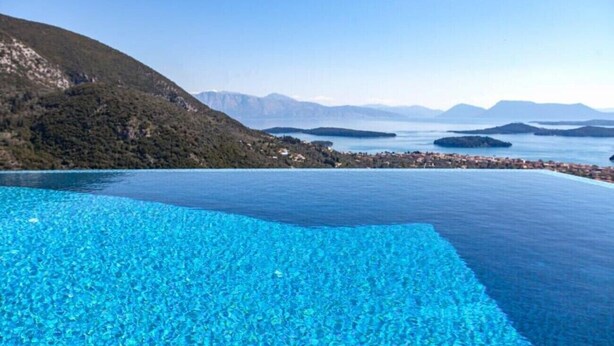 Una piscina infinita de color azul intenso, con vistas a un paisaje montañoso y a islas lejanas.