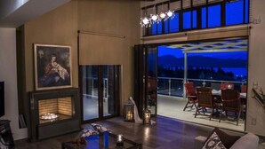 A modern living room with a fireplace, a dining area with a table and chairs, and a large sliding glass door leading to an outdoor patio.