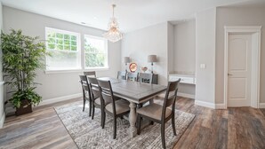 A dining room with a wooden table, six chairs, a chandelier, a potted plant, and a large window. - Beautiful Valley Farm House, With View (Puyallup)