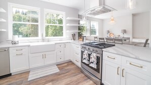 A modern kitchen with white cabinetry, a stainless steel stove, and large windows offering a view of greenery. - Beautiful Valley Farm House, With View (Puyallup)