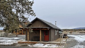 A rustic wooden cabin with a red door, a porch, and a satellite dish.