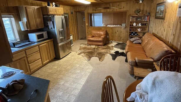 A cozy cabin interior with wooden walls, a leather sofa, a dining table, and a kitchen area with a refrigerator and microwave.