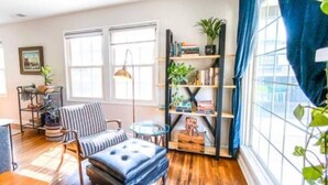 A room with a wooden floor, a striped chair, a small table, a bookshelf, and a window with blue curtains. - Chic Boho Getaway Near Downtown Visalia (Visalia)