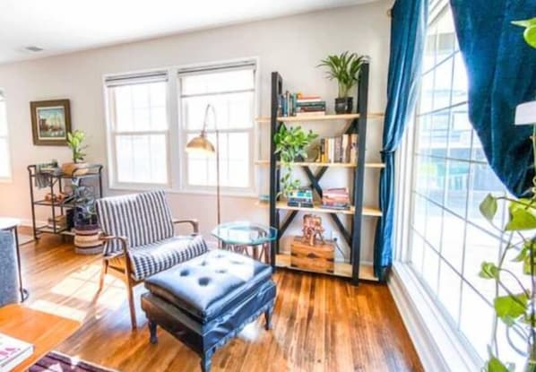 A room with a wooden floor, a striped chair, a small table, a bookshelf, and a window with blue curtains. - Chic Boho Getaway Near Downtown Visalia (Visalia)