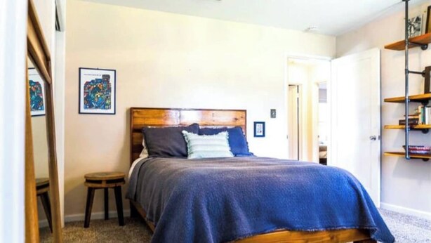 A bedroom with a wooden bed, a small stool, a door, and a shelf with books. - Chic Boho Getaway Near Downtown Visalia (Visalia)