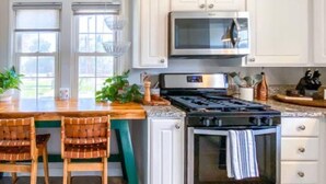 A kitchen with white cabinets, a stove, an oven, and a microwave. There are two wooden chairs and a table with plants. - Chic Boho Getaway Near Downtown Visalia (Visalia)