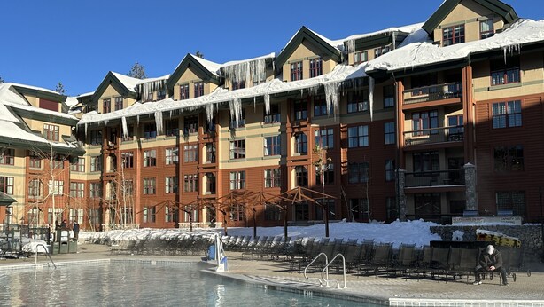 Ein Hotel mit Pool, schneebedeckten Dächern und blauem Himmel.