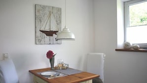 Un coin repas avec une table en bois, des chaises blanches, un luminaire suspendu et une fenêtre donnant sur un paysage verdoyant.