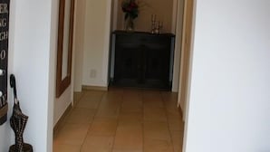 Un couloir doté d’un sol carrelé, une console sombre ornée d’un vase et de bougies, et un miroir encadré sur le côté gauche.