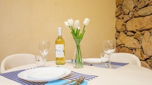 Una mesa redonda de comedor con platos, cubiertos, una botella de vino y un jarrón con flores blancas.