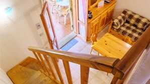 Una escalera de madera conduce a una habitación con un sofá a cuadros, una mesa de madera y vistas a un comedor con sillas y una mesa.