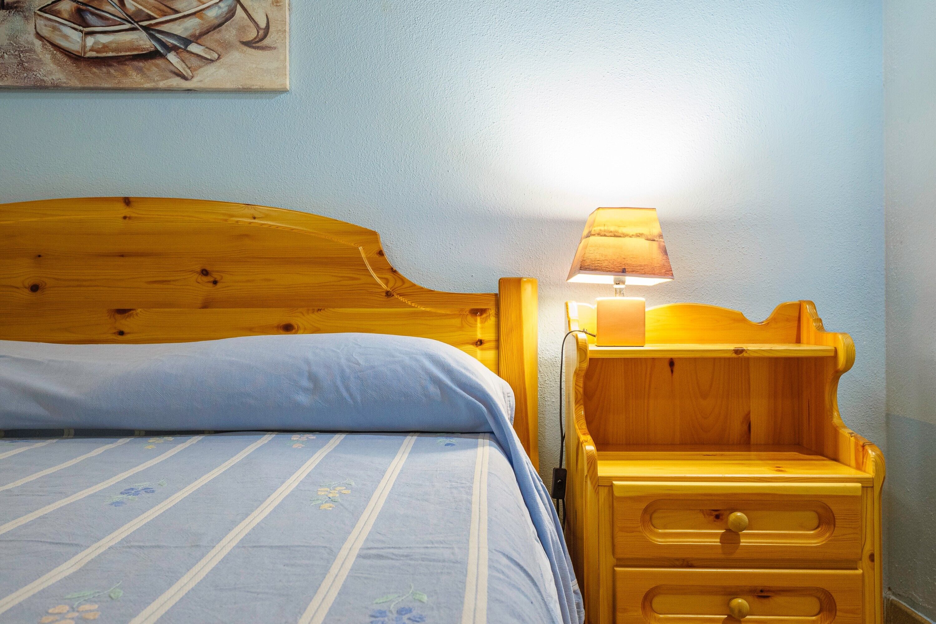 A wooden bed with a headboard, a bedside lamp, and a wooden nightstand with drawers.