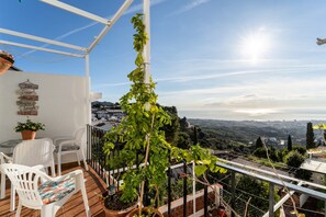 Ein Balkon mit weißen Stühlen, einem Blumentopf und Blick auf eine Stadtlandschaft.