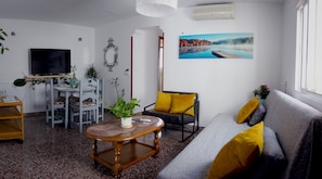 A living room with a sofa, a coffee table, a TV, a dining table with chairs, and a painting on the wall.