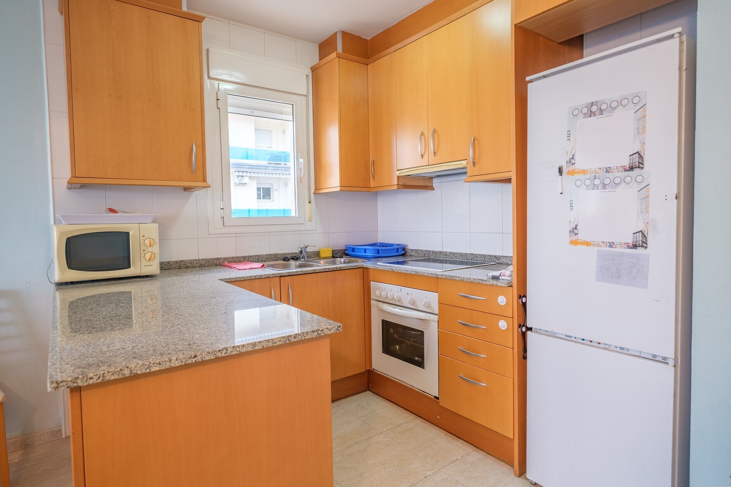A kitchen with wooden cabinets, a microwave, an oven, a refrigerator, and a window.