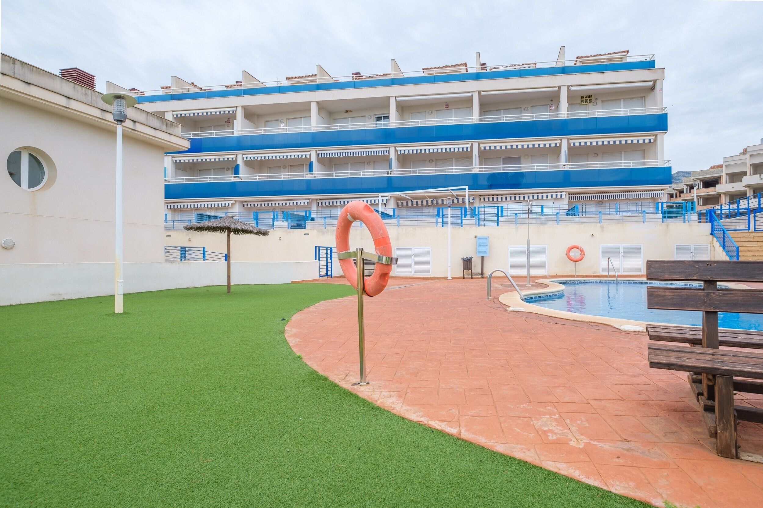 Una zona de piscina con un flotador salvavidas, un banco y un edificio con varios balcones.