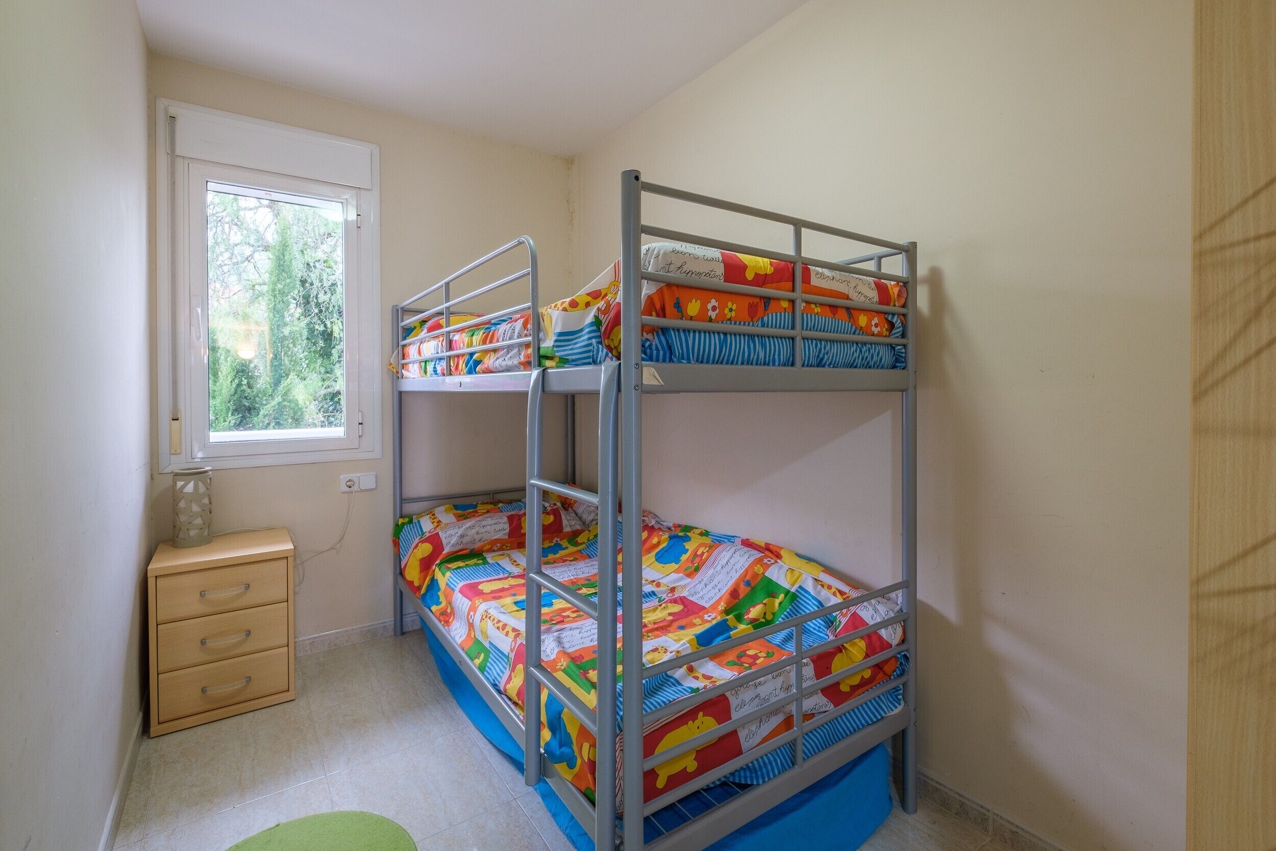 A bunk bed room with a window, a small drawer unit, and a green rug.